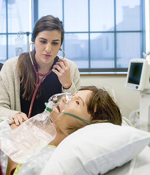 Female student uses stethoscope to listen to mannikin in the simulation lab