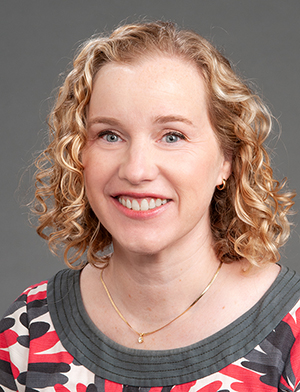 Head shot of woman with blonde curly hair not quite shoulder length and wearing a gray, white and red top