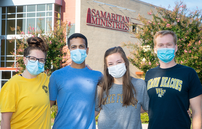 Two young men and two young women, all wearing face masks, stand outside a Samaritan Ministries building