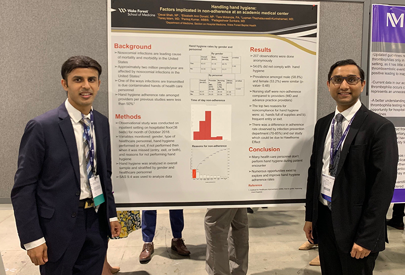 Two men in suits stand in front of a research poster with a red bar graph