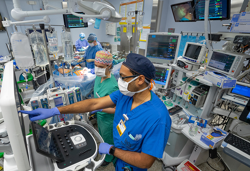 Two people, one in green scrubs and one in blue, stand in a room surrounded by medical equipment