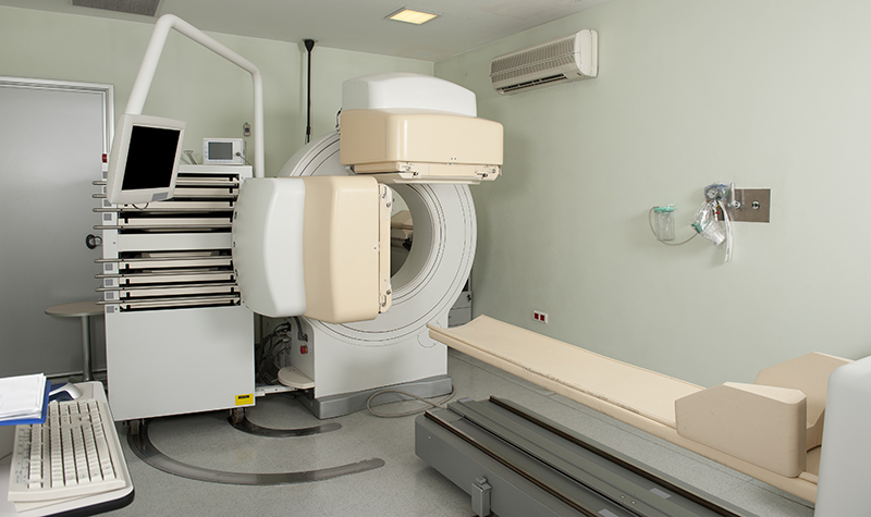 An off-white room with large medical equipment, including one that looks like a giant doughnut and one that looks like a cot