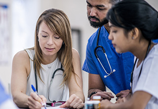 Two women and one man look down at a notepad and medicine bottles