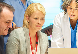 Two women and one man in business attire look at a laptop