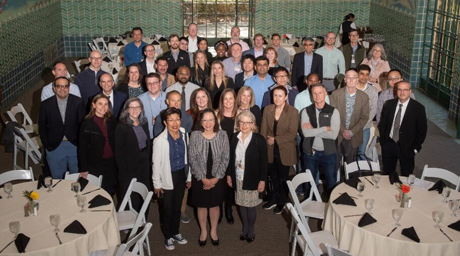 A group of students and faculty gather in the back of a banquet hall for a group photo at the Immuno-Oncology Retreat.