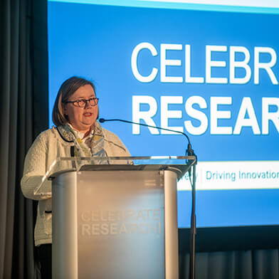 A woman stands at a podium giving a presentation for Celebrate Research.